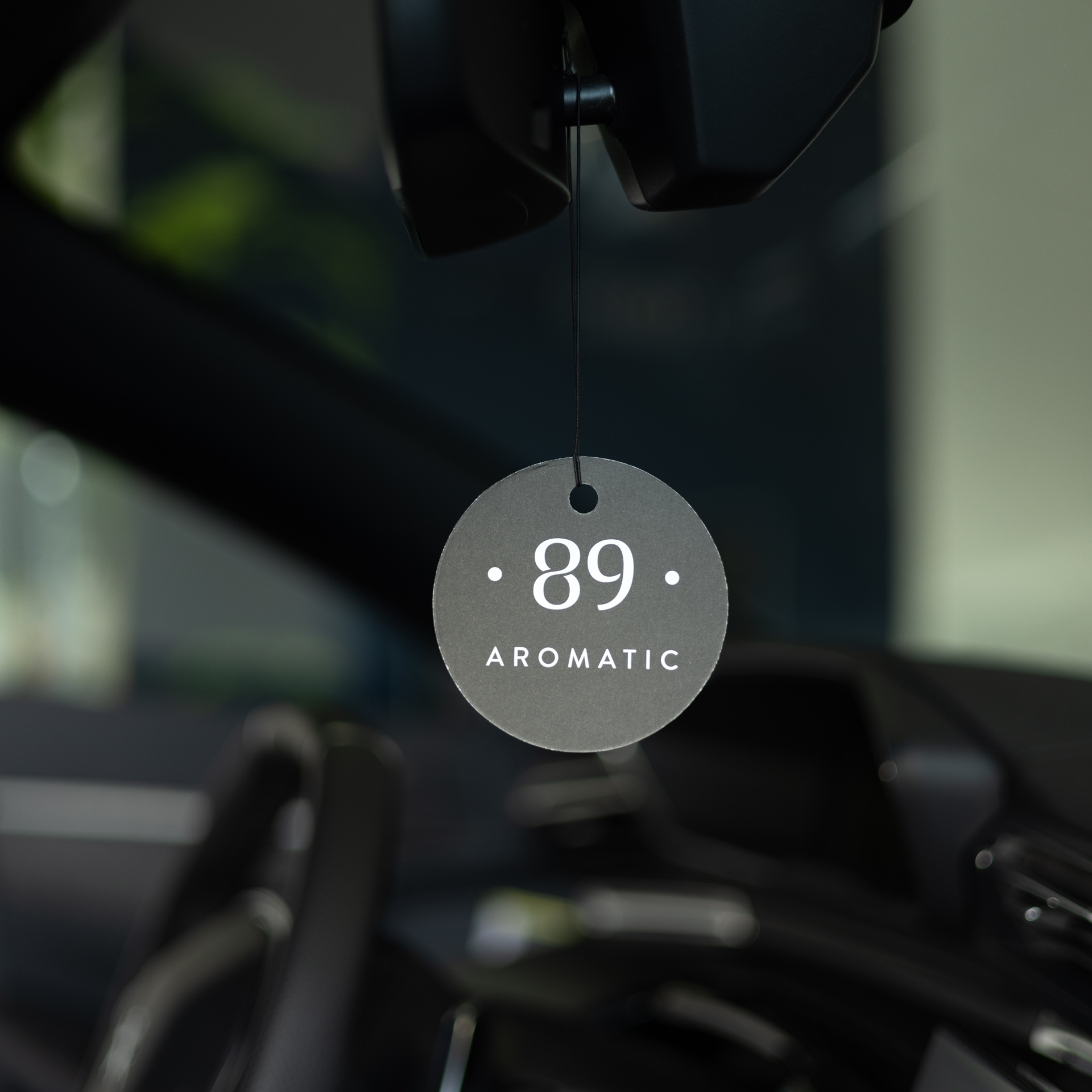 Pendente aromático cinza com texto 89 AROMATIC pendurado no espelho retrovisor do carro.