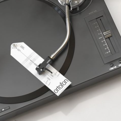 Toca-discos preto com braço metálico e etiqueta ortofon, chávena branca ao lado