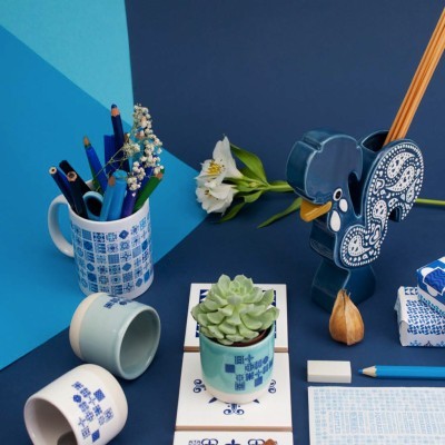 Conjunto de canecas e objetos de porcelana azul e branco com padrões geométricos e florais sobre mesa azul
