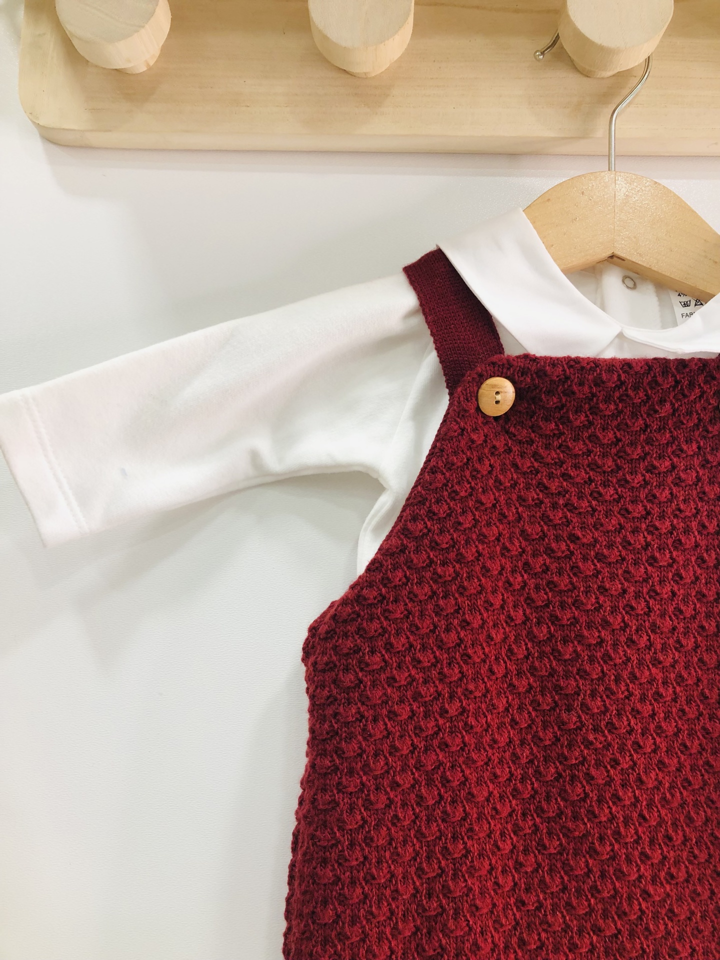 Roupa de bebé com vestido vermelho de malha e camisa branca pendurada num cabide de madeira