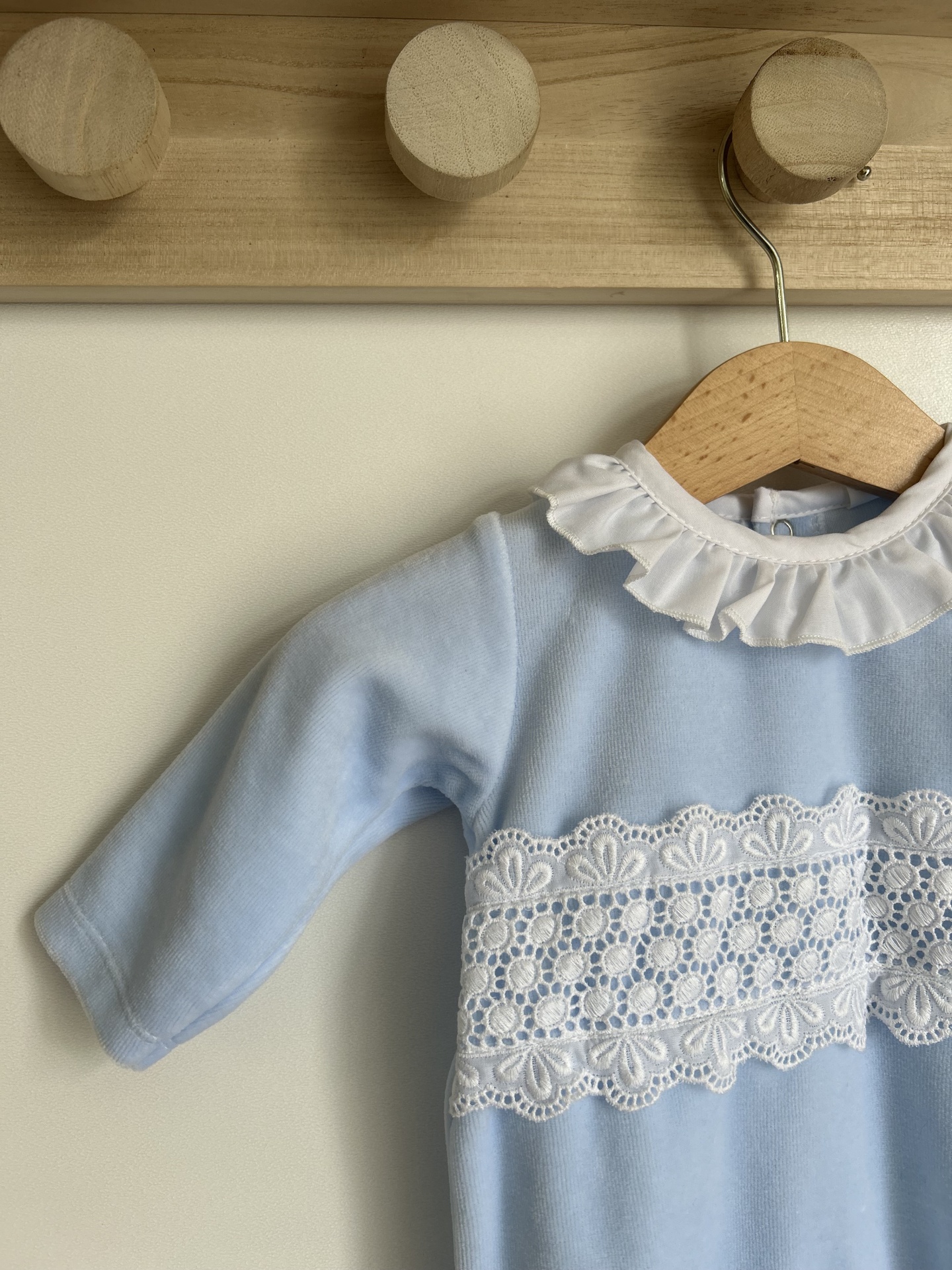Vestido azul claro infantil com gola branca e renda pendurado em cabide de madeira.