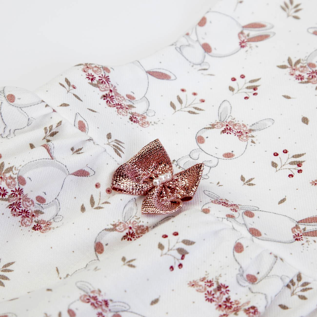 Pano branco com coelhos e flores, e laço rosa brilhante no centro