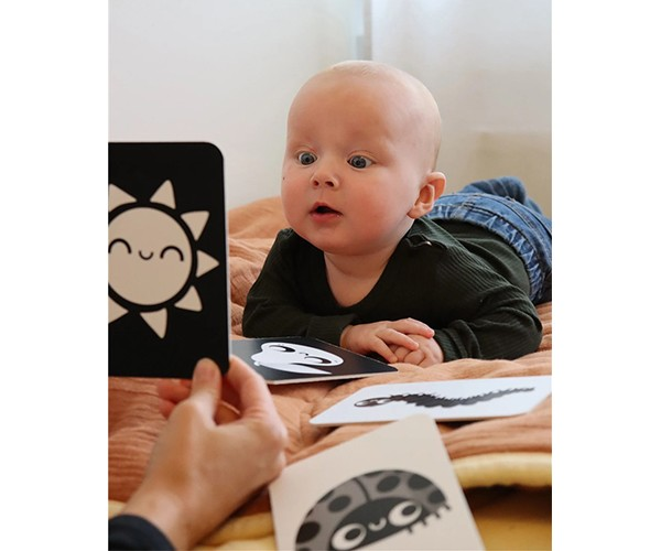 Cartões educativos preto e branco com bebé de bruços numa cama laranja