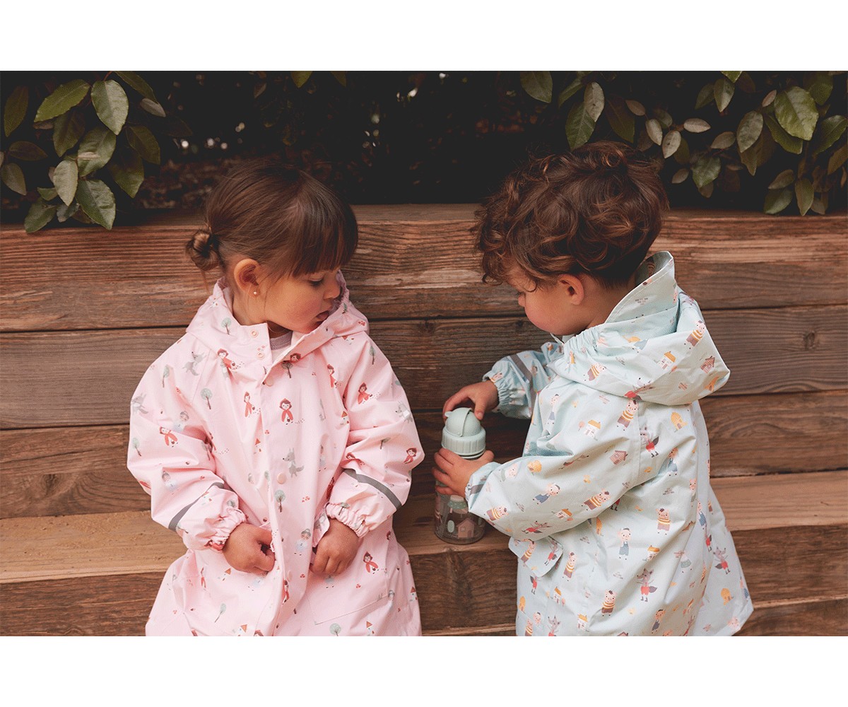 Crianças com impermeáveis rosa e azul claro com capuz sentadas num banco de madeira