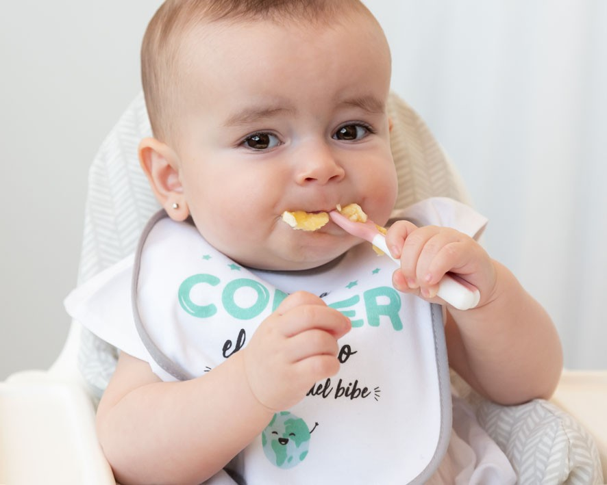 Bebé a comer com babete branco e cadeira de bebé cinzenta