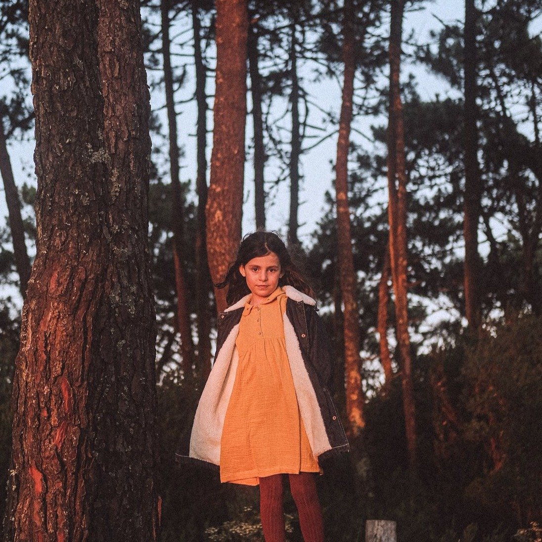 Menina com vestido amarelo claro e casaco branco numa floresta