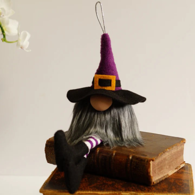 Boneco pendurável de bruxa com chapéu roxo e preto e pernas às riscas sentado em livros antigos