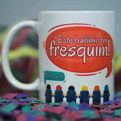 Caneca branca com texto e figuras coloridas sobre confetes
