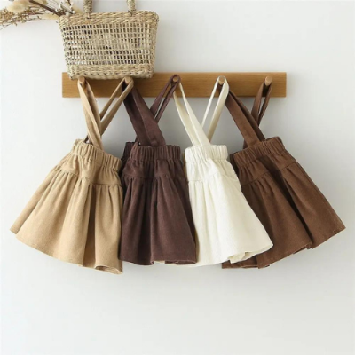 Quatro saias para crianças de cores bege, castanho, branco e castanho escuro penduradas num cabide de madeira