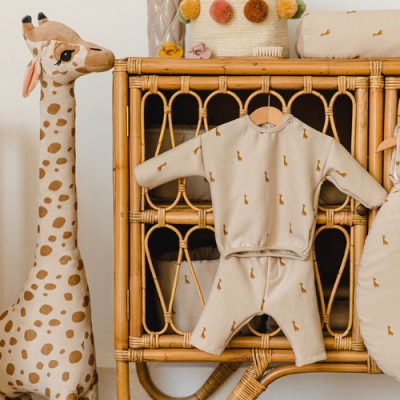 Roupa de bebê bege com padrão de girafas e brinquedo de peluche girafa