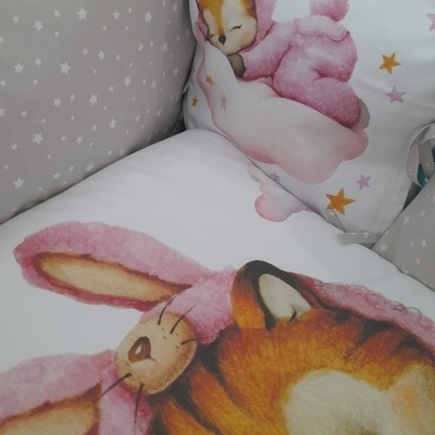Roupa de berço com desenhos de animais em pelúcia rosas e castanhos, almofadas e proteção cinzentas com estrelas brancas