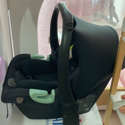 Cadeira auto de bebé preta com detalhes verde, sobre caixa BABY NAT' com desenho de urso.