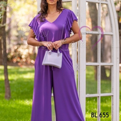 Mulher a usar macacão roxo com mala lilás junto a estrutura de madeira e vidro branca e relva verde.