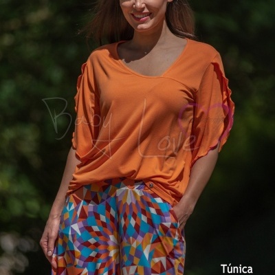 Mulher com túnica laranja e calças coloridas com padrão geométrico em ambiente exterior