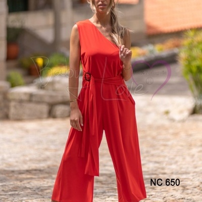 Mulher com macacão vermelho de tecido fluido, com cinto e decote assimétrico, em ambiente exterior com chão de calçada.