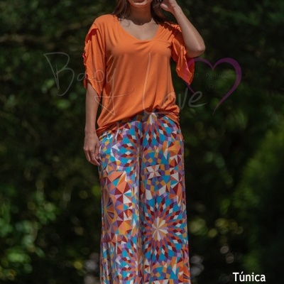 Mulher com túnica laranja e calças largas coloridas em ambiente exterior