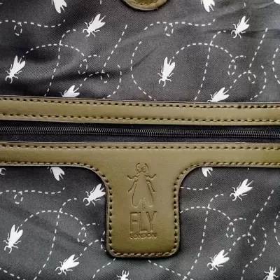 Bolsa preta com padrão de insetos brancos e detalhes em pele verde com logotipo Fly London.
