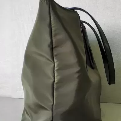 Mala verde-oliva em tecido com alças pretas vista de perfil