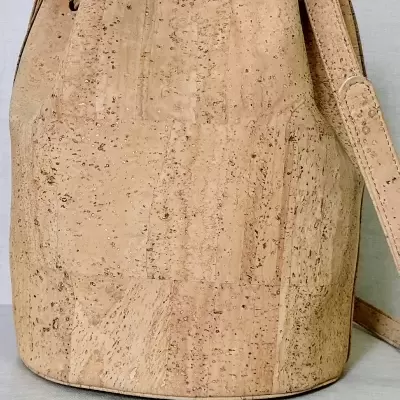 Mala de cortiça bege em forma de saco com alça ajustável sobre tecido cinza claro