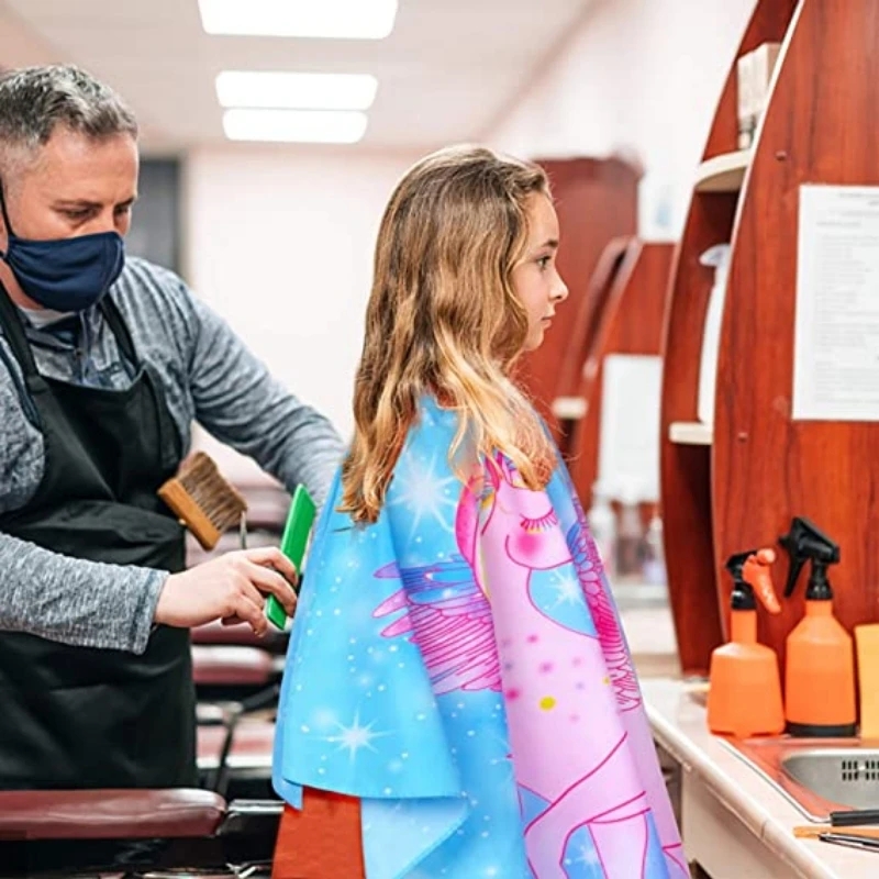 Criança com capa de corte com estampas de unicórnio em salão de beleza