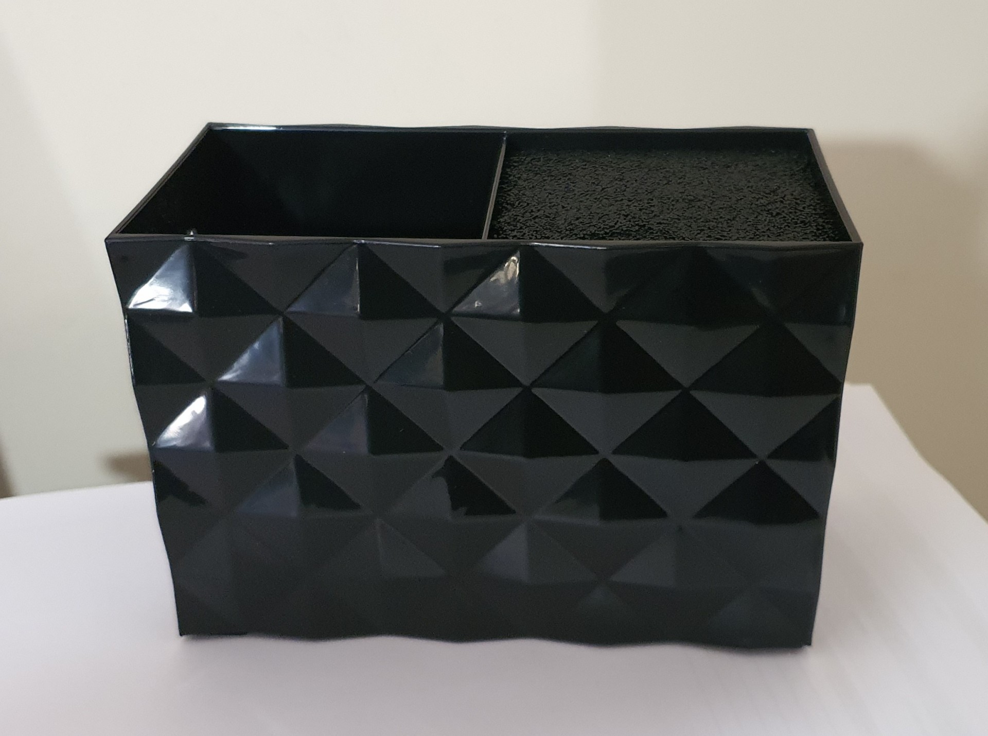 Organizador preto de plástico com duas secções, relevo triangular e esponja preta numa das secções.