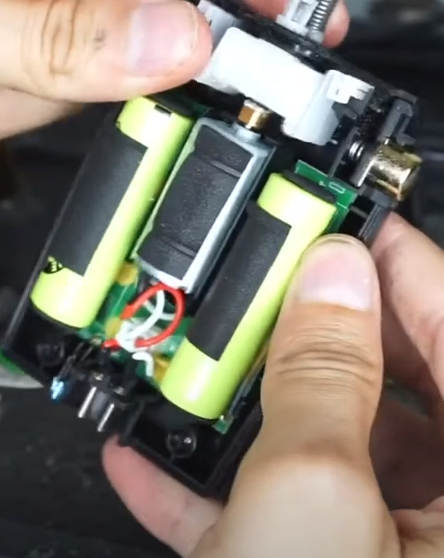 Dispositivo eletrônico com baterias recarregáveis verdes, motor e fios, nas mãos de uma pessoa.