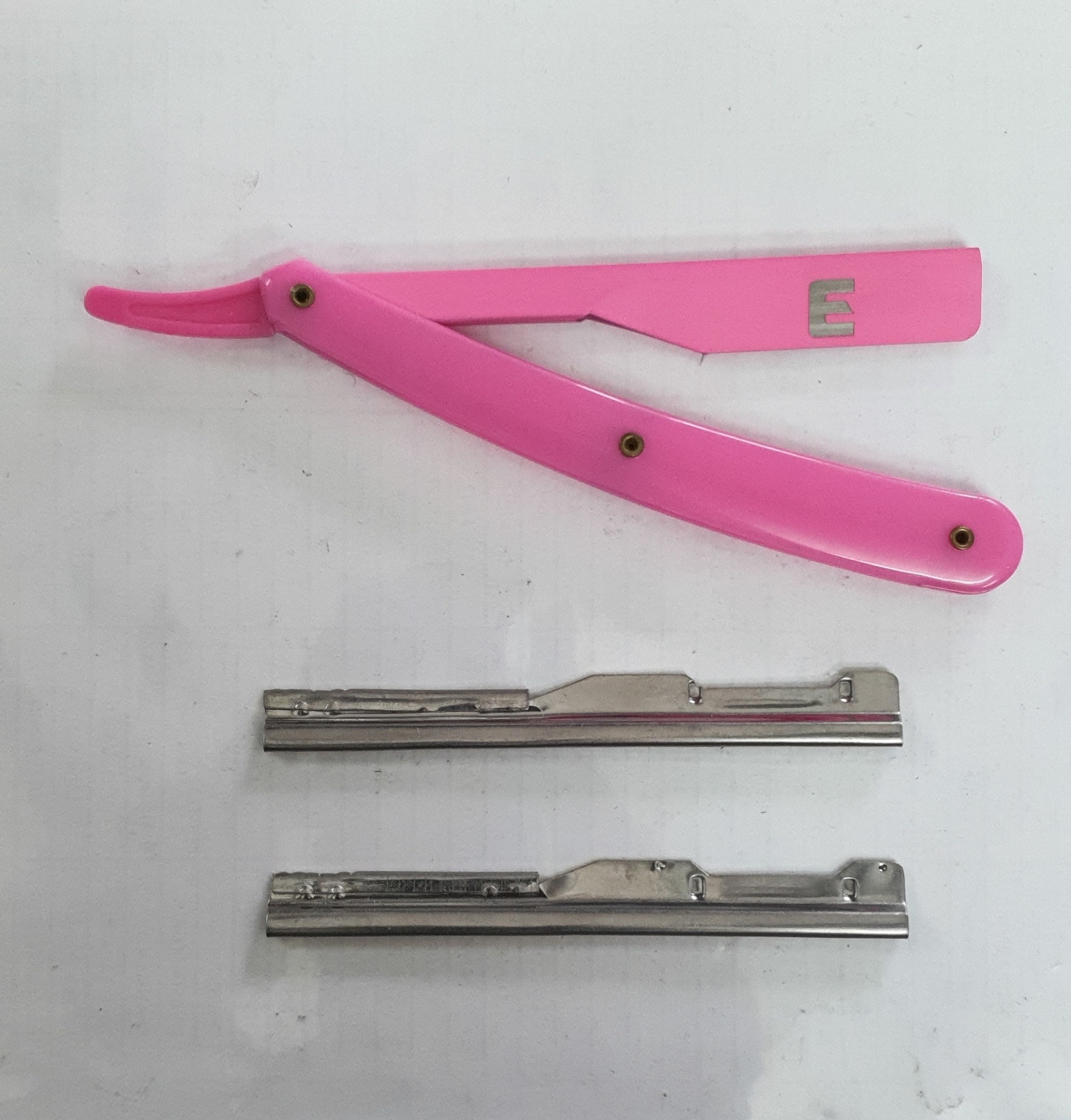 Navalhete rosa com lâminas metálicas sobre superfície branca