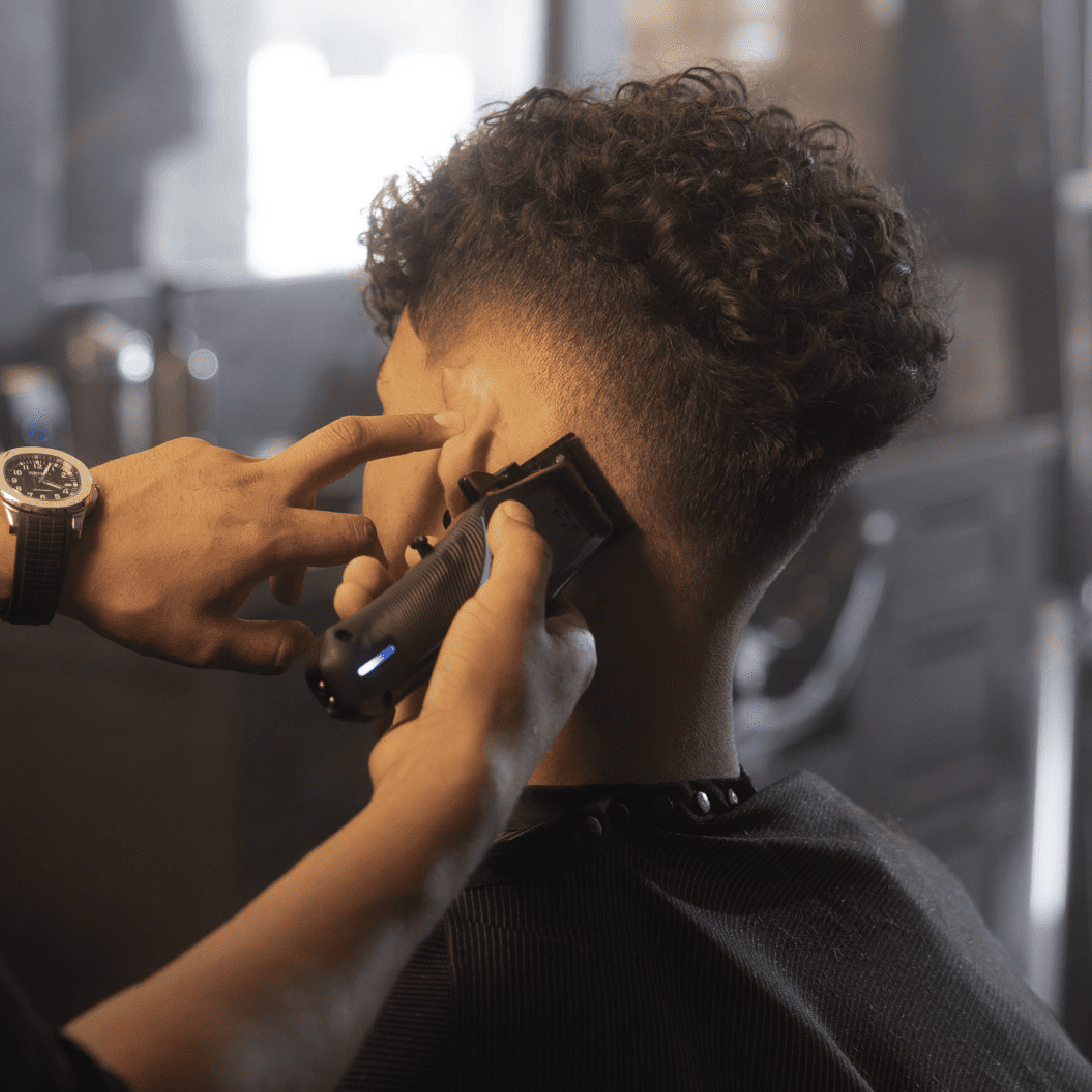 Pessoa com cabelo encaracolado a receber corte com aparelho de cortar cabelo preto em barbearia