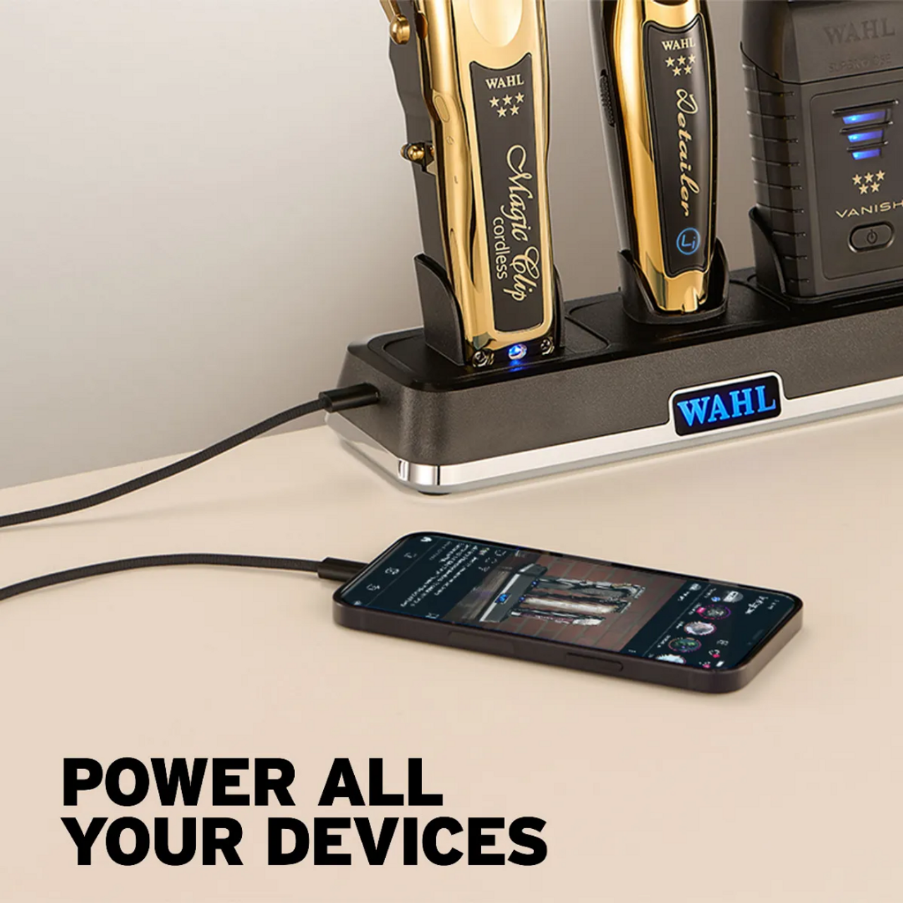 Base de carregamento Wahl com aparadores dourados e smartphone a carregar em fundo claro com texto 'POWER ALL YOUR DEVICES'.