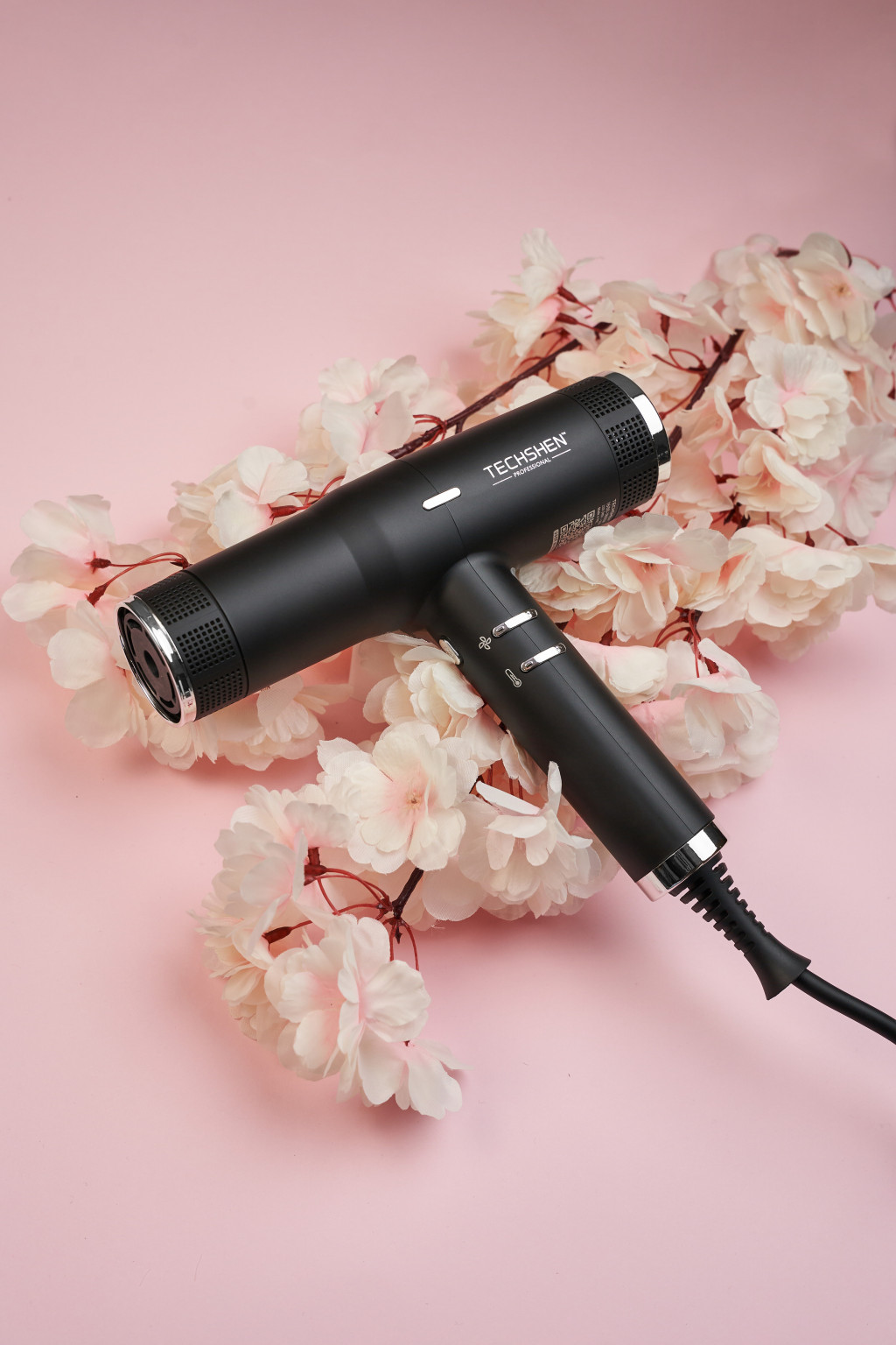 Secador de cabelo preto TECHSHEM sobre flores claras e fundo rosa