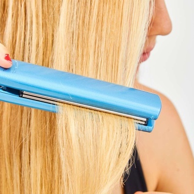 Mulher a usar prancha alisadora azul em cabelo loiro