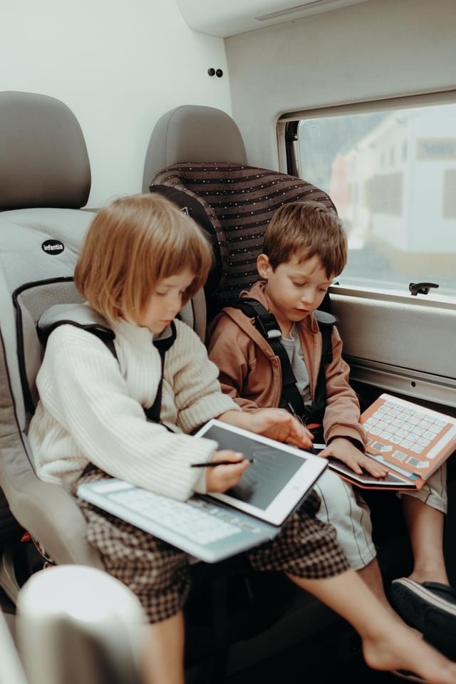 Duas crianças em cadeirinhas de segurança num veículo, ambas com tablets e teclados