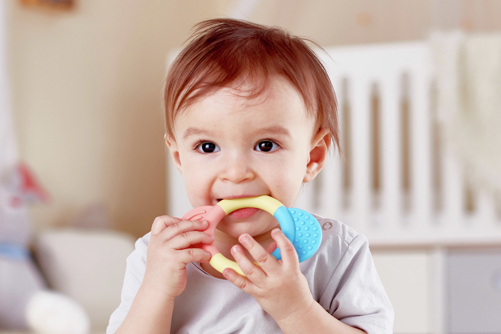 Bebé a morder brinquedo de dentição colorido num quarto de bebé
