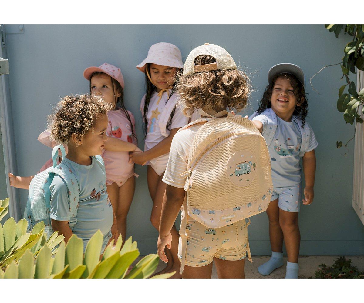 Cinco crianças com roupas coloridas e chapéus em espaço exterior com paredes azuis e plantas