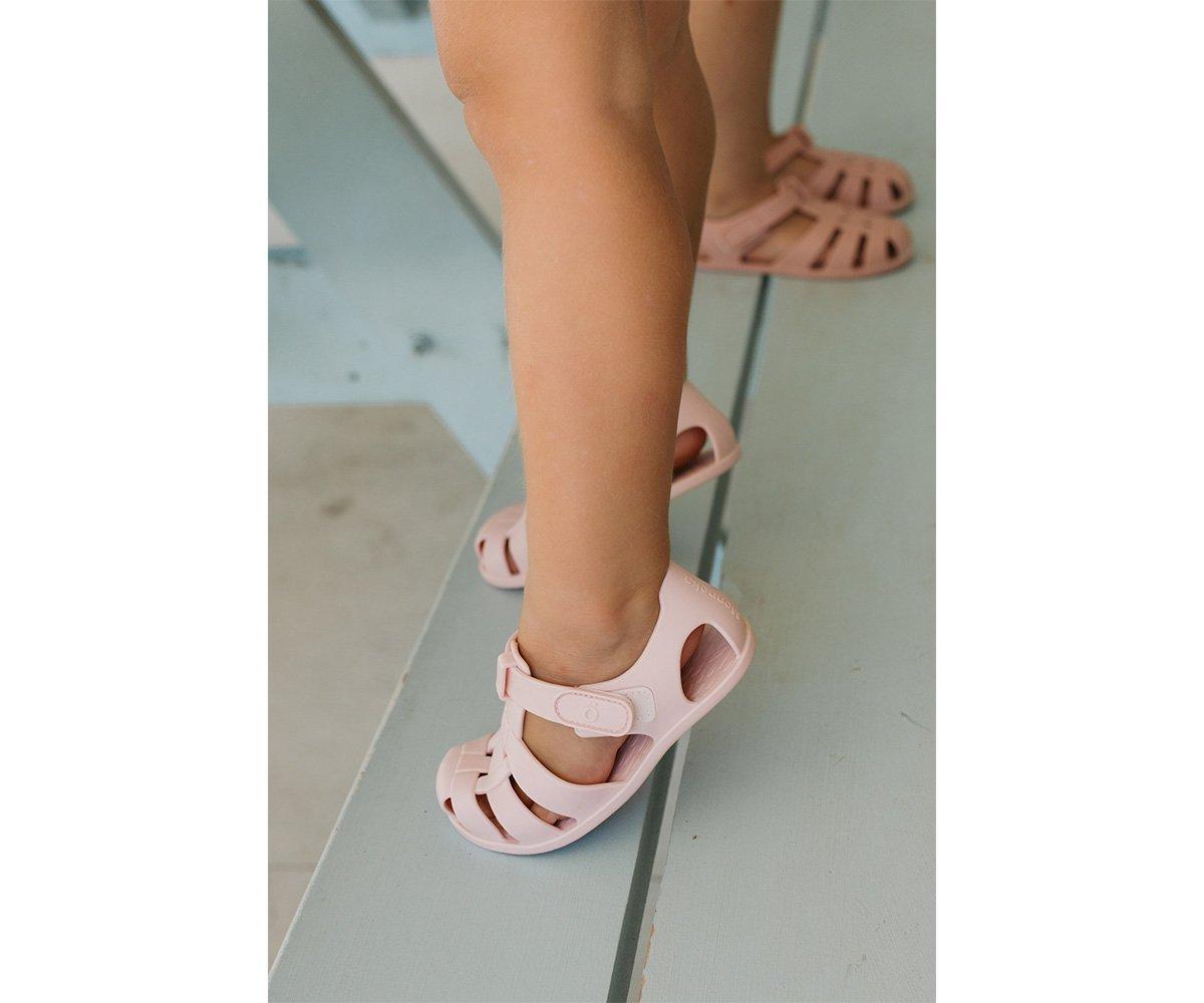 Sandálias cor de rosa para criança em chão claro junto a espelho