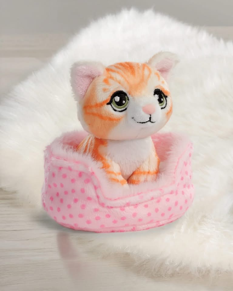 Pelúcia de gatinho laranja sentado em cama rosa com pontos sobre superfície clara e tecido felpudo branco