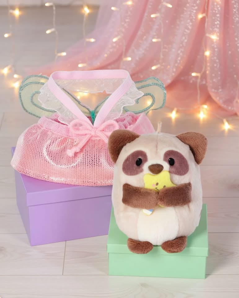 Pelúcia de animal segurando brinquedo em caixa verde ao lado de caixa roxa com saco rosa e asas decorativas