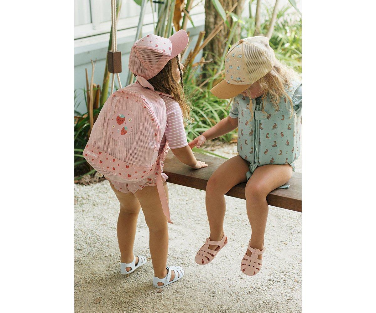 Crianças com mochilas coloridas e bonés, sandálias, ambiente ao ar livre