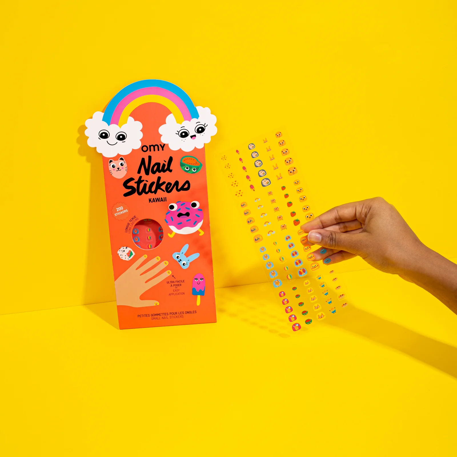 Pacote laranja de autocolantes para unhas com desenhos kawaii e mão a segurar tira transparente com autocolantes.