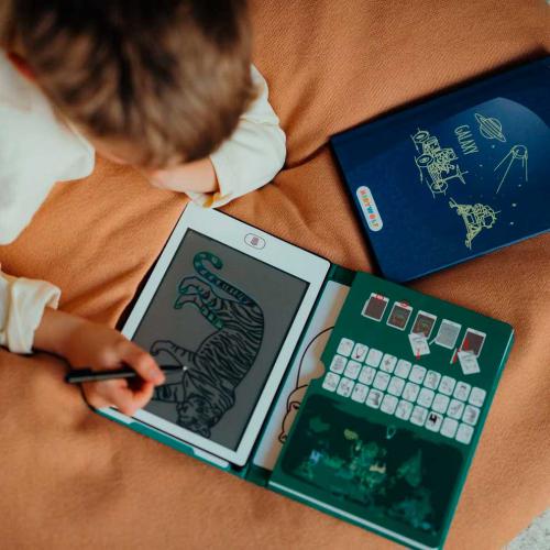 Criança a desenhar num tablet interativo com teclado e blocos, manta castanha e caixa azul ao lado