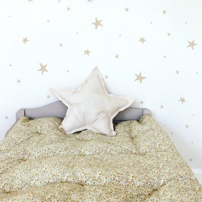 Cama infantil com edredão floral, almofada estrela e decoração de parede com estrelas douradas