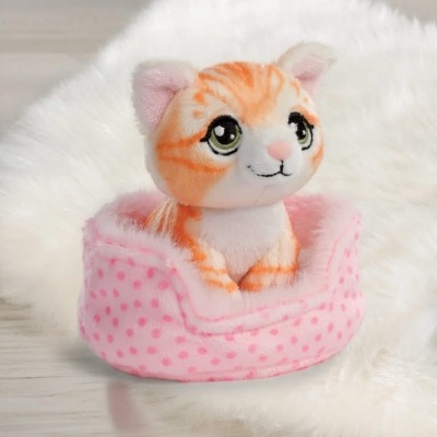 Pelúcia de gatinho laranja sentado em cama rosa com pontos sobre superfície clara e tecido felpudo branco