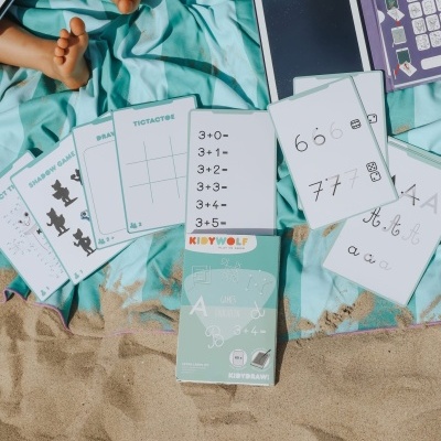 Cartas educativas KIDYWOLF com temas de matemática e escrita numa toalha azul clara na areia
