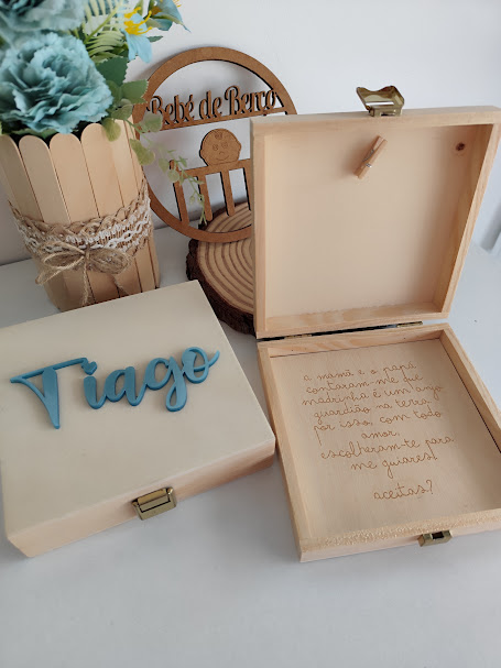 Caixa de madeira com nome e texto gravado, vaso com flores e placa decorativa