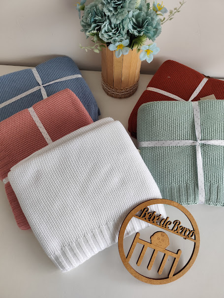 Conjunto de mantas coloridas em tecido de malha com fita branca e decoração com plantas e ornamento de madeira