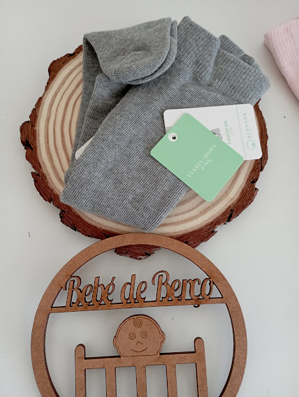 Par de meias cinzentas com etiquetas sobre base de madeira, placa decorativa de madeira com texto 'Bebé de Berço'