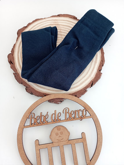 Meias azuis escuras dobradas sobre disco de madeira com ornamento de madeira escrito 'Bebé de Berço'