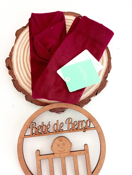 Meias vermelhas de bebé com etiqueta verde sobre tábua de madeira, emblema de madeira com texto Bebé de Berço e desenho de bebé.