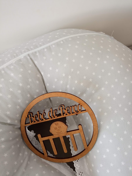 Almofada cinza com estrelas brancas e enfeite redondo de madeira com texto 'Rede de Berço'