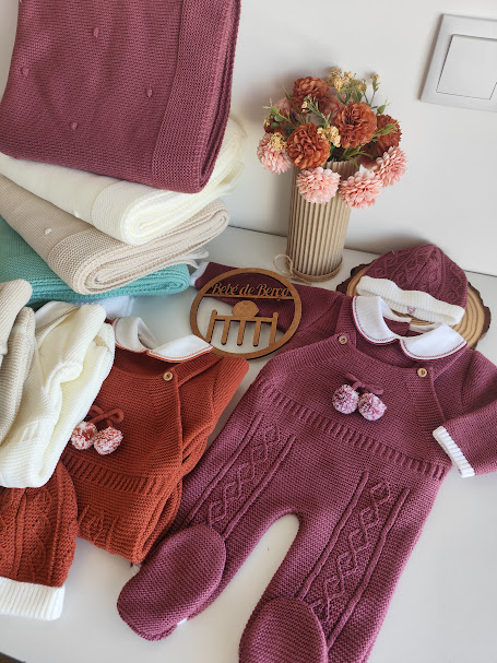 Roupa de bebé em malha bordeaux e castanho com mantas e vaso de flores secas